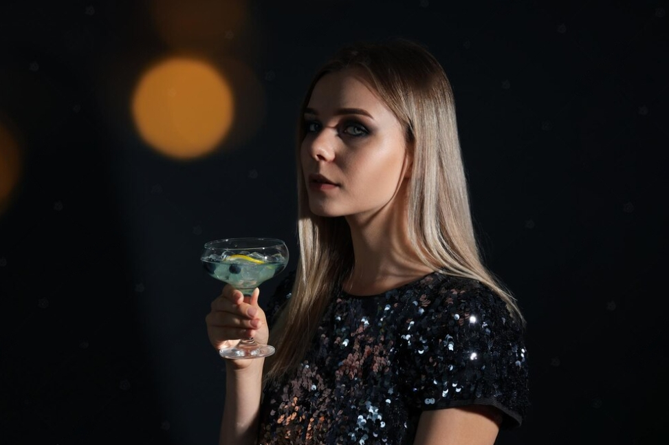 woman in a shiny black dress with a cocktail in her right hand on a black background