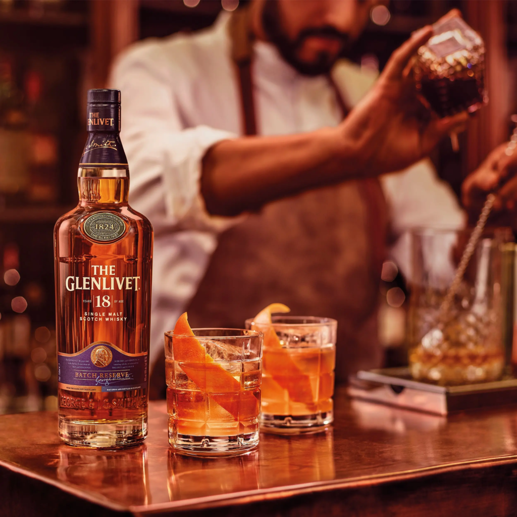 The bartender is preparing a cocktail, in the foreground is a bottle of scotch