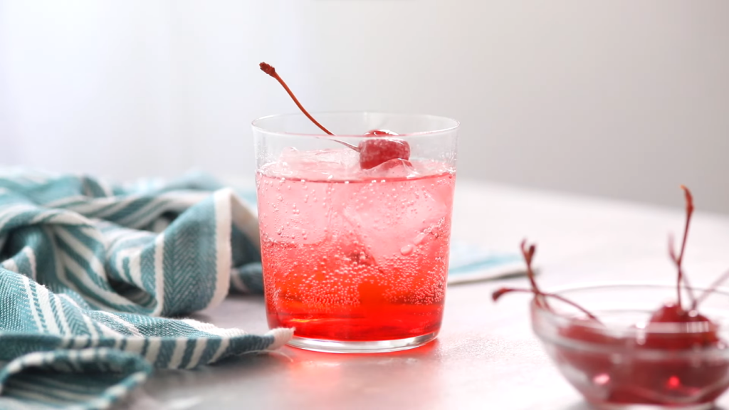 a glass with a cocktail decorated with a cherry, towel and glass bowl with cherries