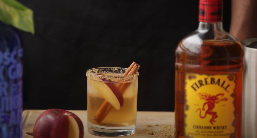 A whiskey glass with apple and cinnamon, and a bottle of Fireball whiskey placed on the side