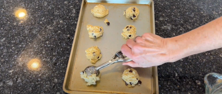 A hand placing cookie dough on a baking pan