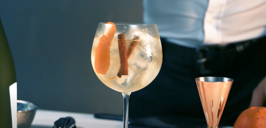 A cocktail in a wine glass with cinnamon and tonic