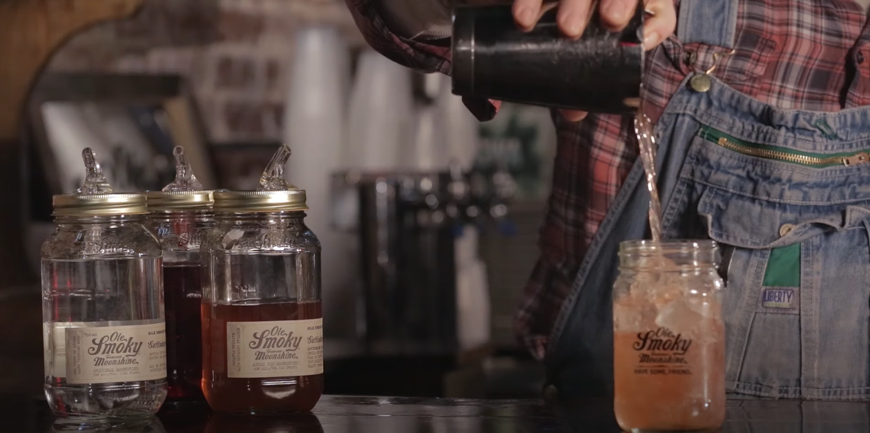 Jars of Ole Smoky Apple Pie Moonshine, with someone pouring a drink into one jar