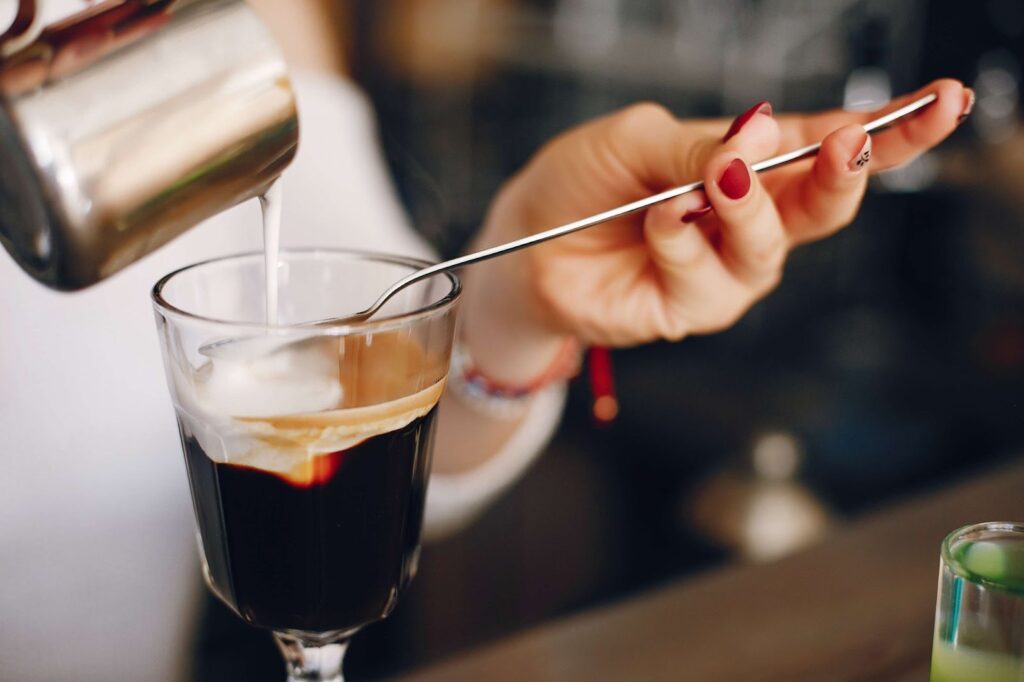 A woman adds cream to a cocktail