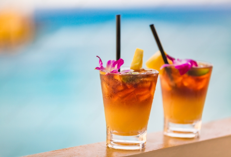 mai tai drinks decorated with flowers on the table near the beach