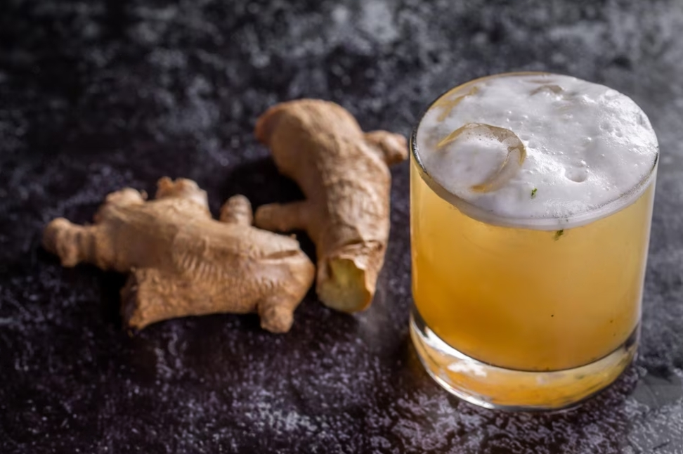 cocktail in a glass with foam and ginger on a black surface