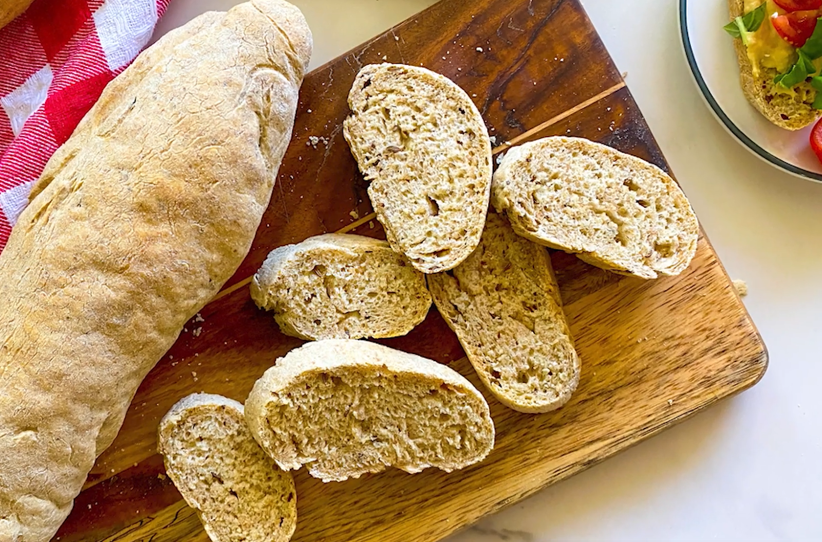 sliced bread lies on a wooden board, plate with meal and red towel on the table