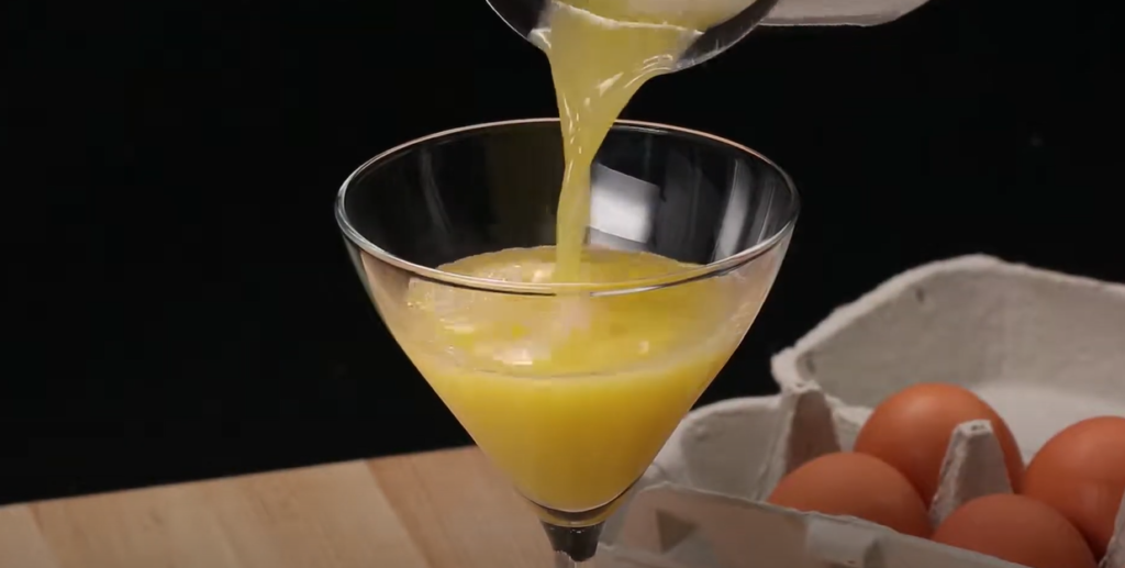 A wine glass with a cocktail being poured into it